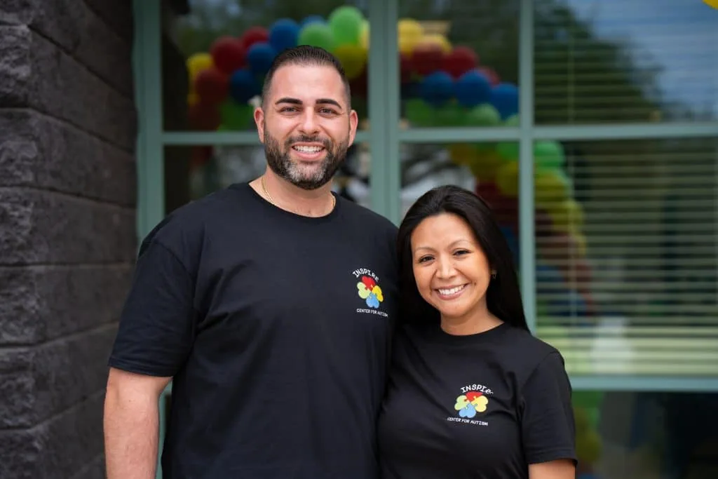 The owners of Inspire Center for Autism in branded shirts outside the Mesa center, with a balloon arch behind them