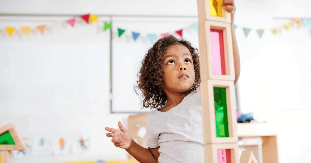 A young child concentrating while stacking colourful wooden blocks during play-based learning