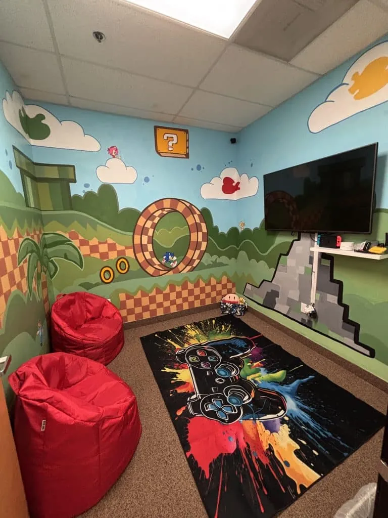 A leisure room painted with video-game murals, a wall-mounted television with a games console, red bean bags and a games-controller rug