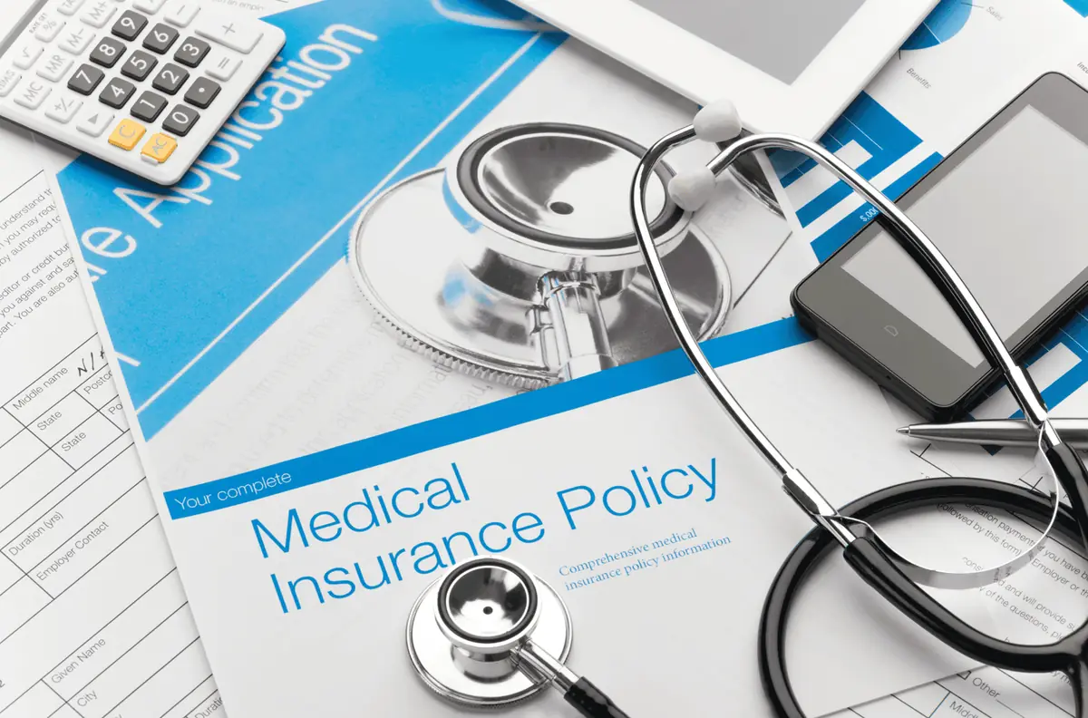 A medical insurance policy document on a desk with a stethoscope, calculator and application forms